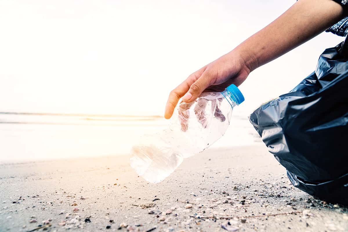 Mensch hebt Plastikflasche am Strand auf