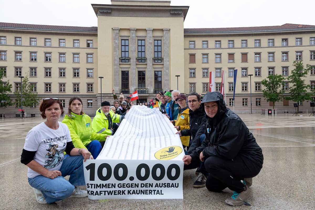 Auf dem Bild sind zahlreiche Menschen in der Hocke zu sehen, die eine riesige Rolle voller Unterschriften halten. Im Hintergrund ist der Innsbrucker Landhausplatz zu sehen.